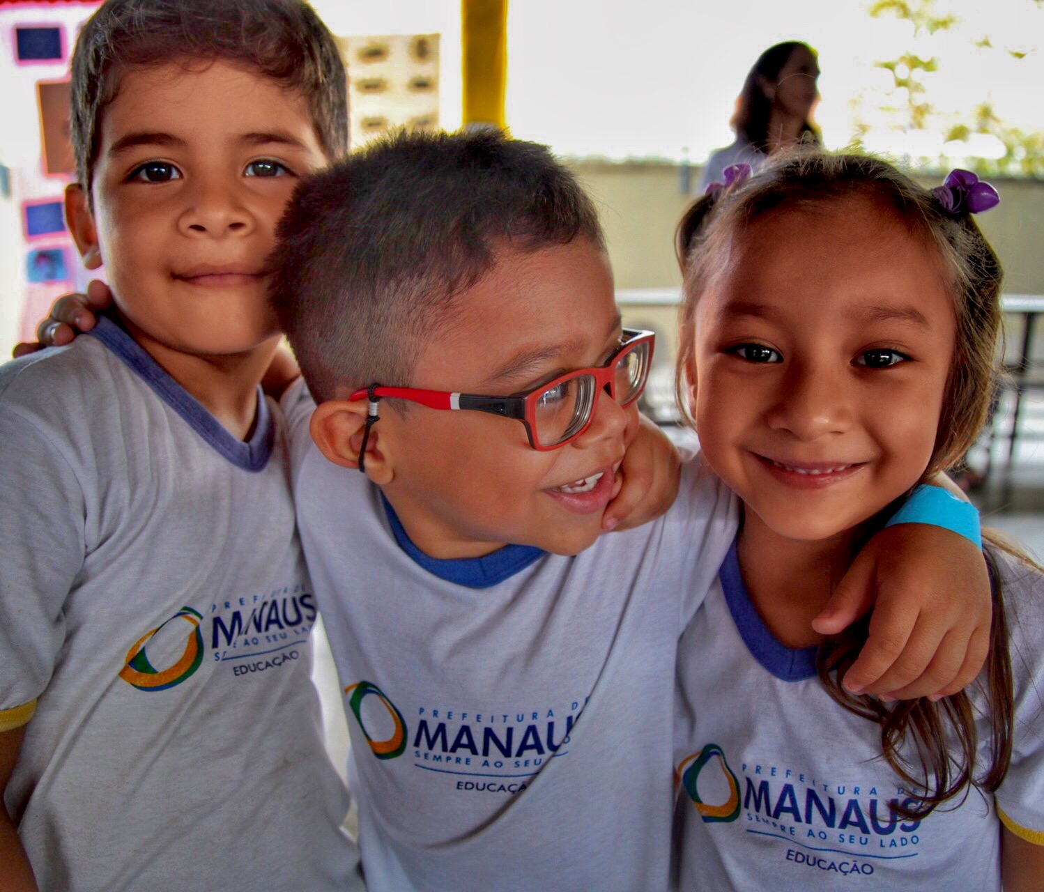 Três alunos sorridentes, com e sem deficiência, posam abraçados.