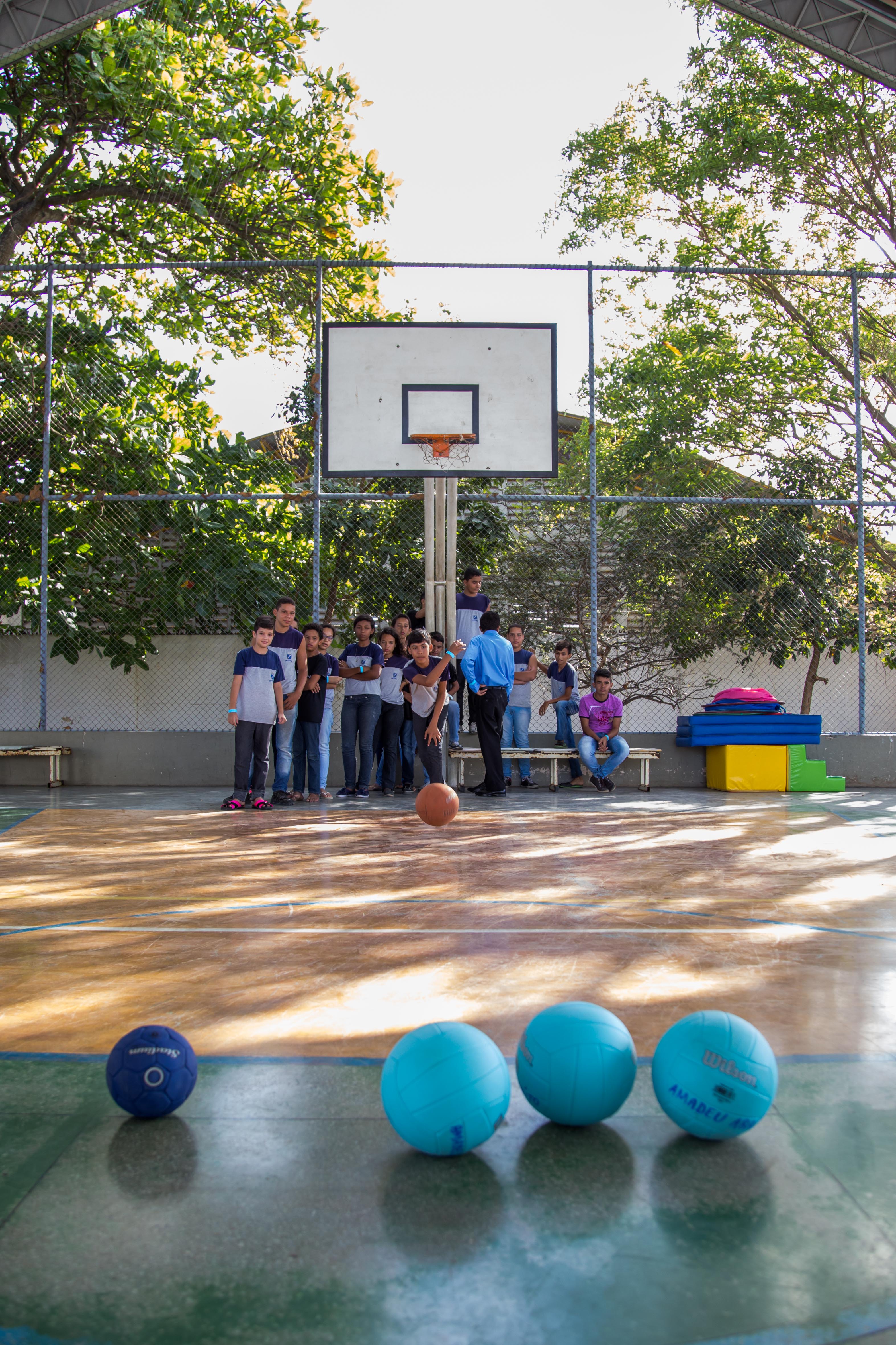Grupo de estudantes joga bilocha em uma quadra de esportes. 