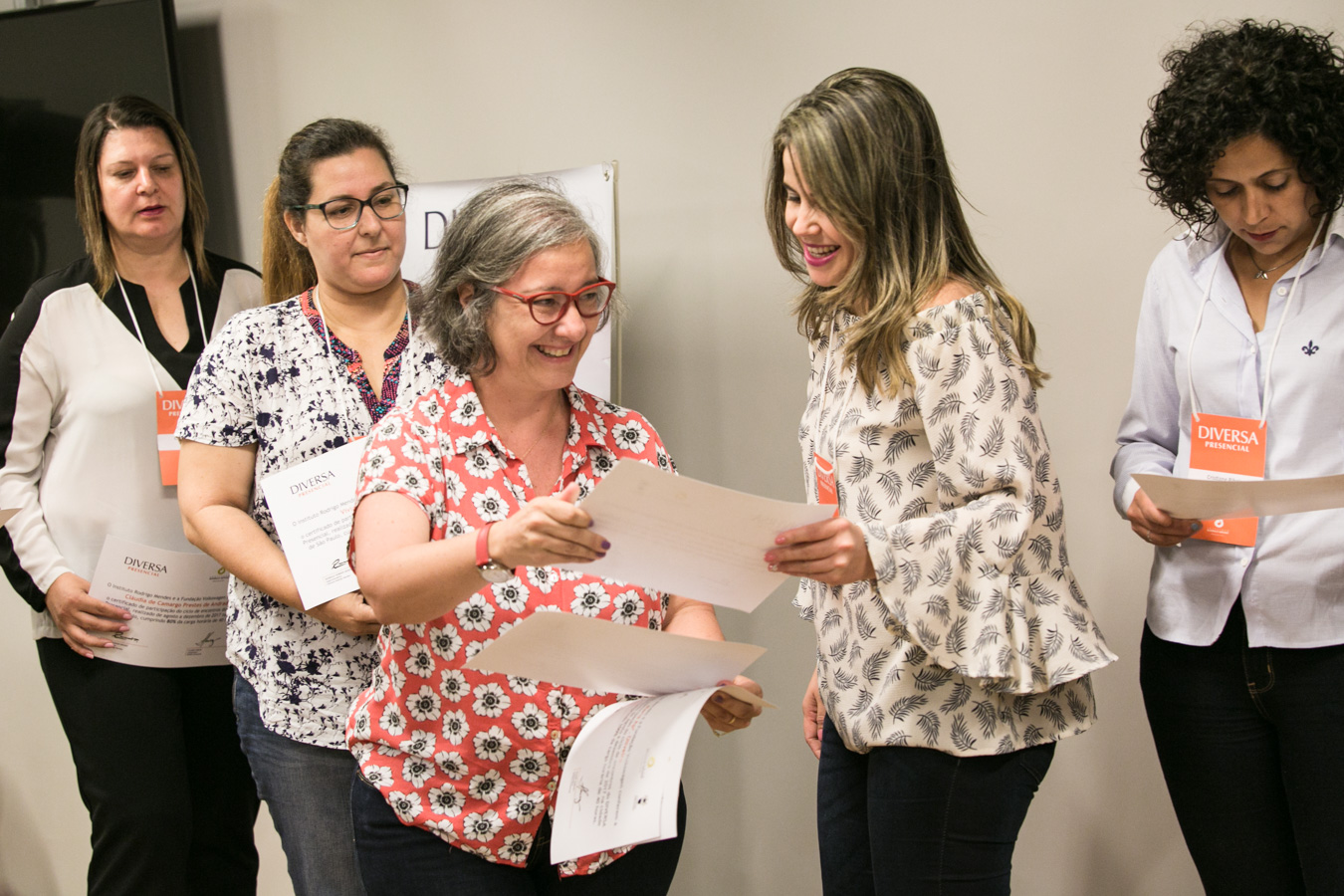 No centro da imagem, uma mulher sorridente entrega um certificado a uma das participantes do DIVERSA Presencial 2017. Ao lado delas, outras mulheres seguram seus certificados.