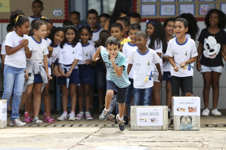 Durante atividade em quadra, um menino corre enquanto é observado por um grupo de crianças. Fim da descrição.