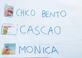 Folha sulfite com imagens de personagens da Turma da Mônica coladas. Ao lado de cada uma, a criança escreveu "Chico bento", "Cascao" e "Monica"