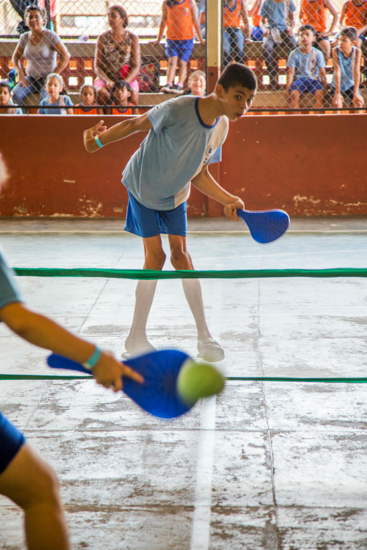 Dois garotos jogam tênis juntos com raquetes feitas de material reutilizável pintado de azul.
