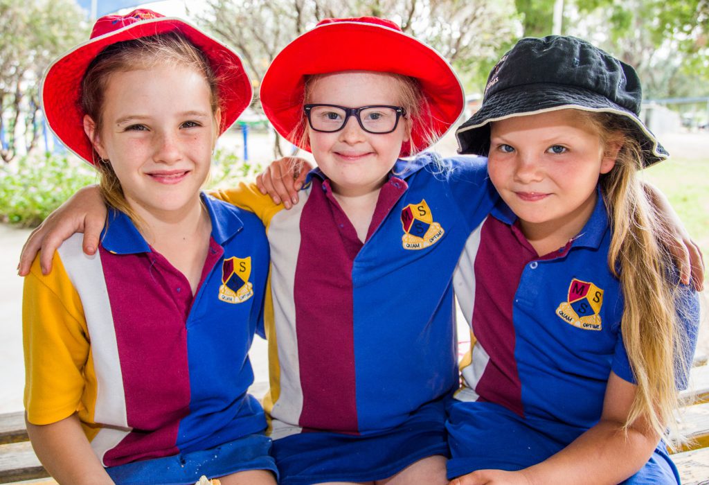 Três meninas posam para fotos abraçadas com uniforme escolar e chapéus. Fim da descrição.