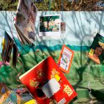 Livros e fotos pendurados em árvore com fitas coloridas. Fim da descrição