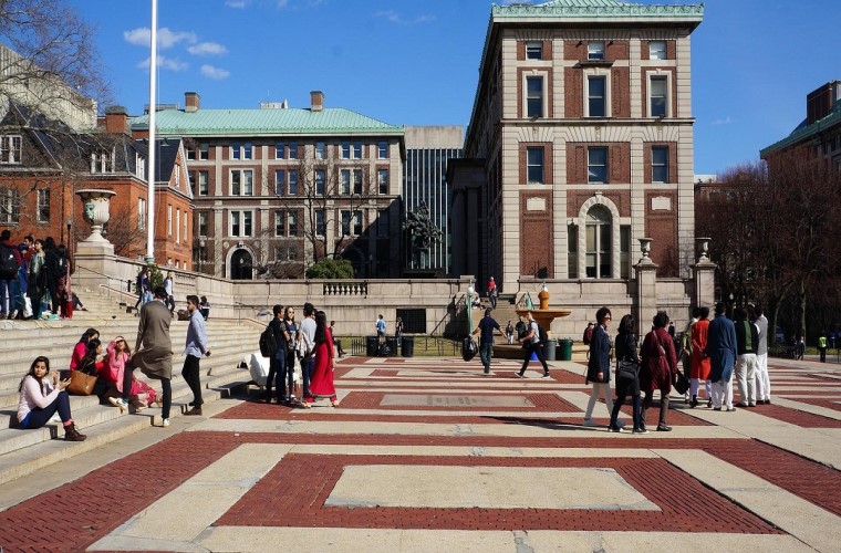 Em frente a prédios da Columbia University, jovens estão em grupos separados no campus. Fim da descrição.