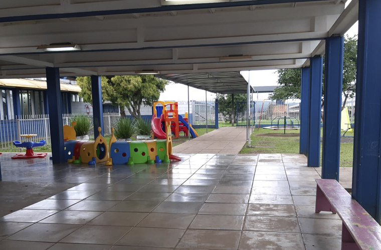 Imagem de local externa da escola onde há alguns brinquedos, como escorregador e gira-gira. Fim da descrição.