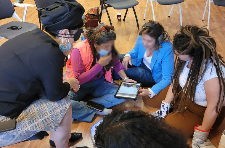 Quatro educadoras estão sentadas em círculo e observam tela de tablet. Fim da descrição. 