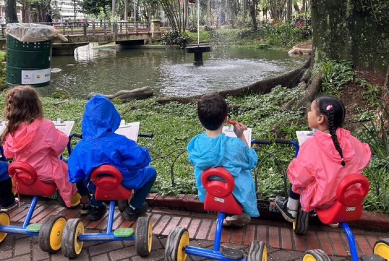 Quatro crianças entre 4 e 5 anos de idade observam o entorno da Praça da República, em São Paulo, e desenham sentados em suas motocas. Fim da descrição. 