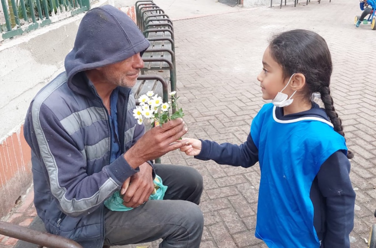 Uma menina entre 4 e 5 anos de idade entrega flores a um homem em situação de rua na Praça da República, em São Paulo. Fim da descrição.
