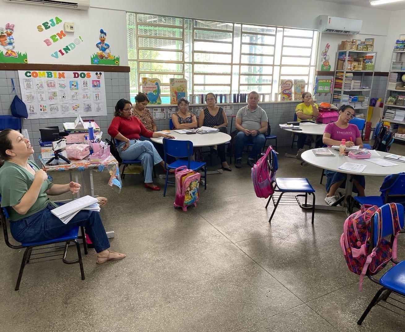 Oito pessoas diversas reunidas em uma sala de aula de educação infantil para encontro formativo. Todas estão sentadas. fim da descrição