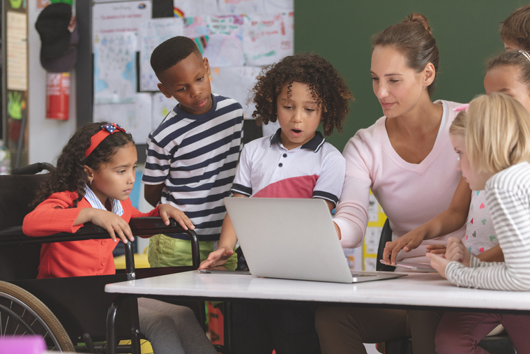 Front view of a teacher and school kids discussing over laptop in classroom at school