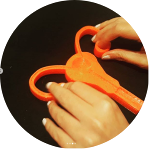 A imagem mostra um aparelho reprodutor feminino impresso em 3D, na cor laranja, sendo tocado por duas mãos. Fim da descrição. 