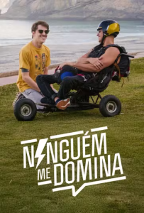 Pôster com a frase "Ninguém me domina" em letras brancas na parte inferior, sobre um gramado verde. Ao fundo, em uma área ao ar livre próxima ao mar e com encostas rochosas, dois homens conversam sorrindo. O homem à direita está sentado em um triciclo adaptado de rodas grandes, vestindo capacete amarelo e preto, óculos escuros e equipamentos de voo livre ou salto. O homem à esquerda está ajoelhado no gramado ao lado dele, usando camiseta amarela, óculos escuros e bigode.